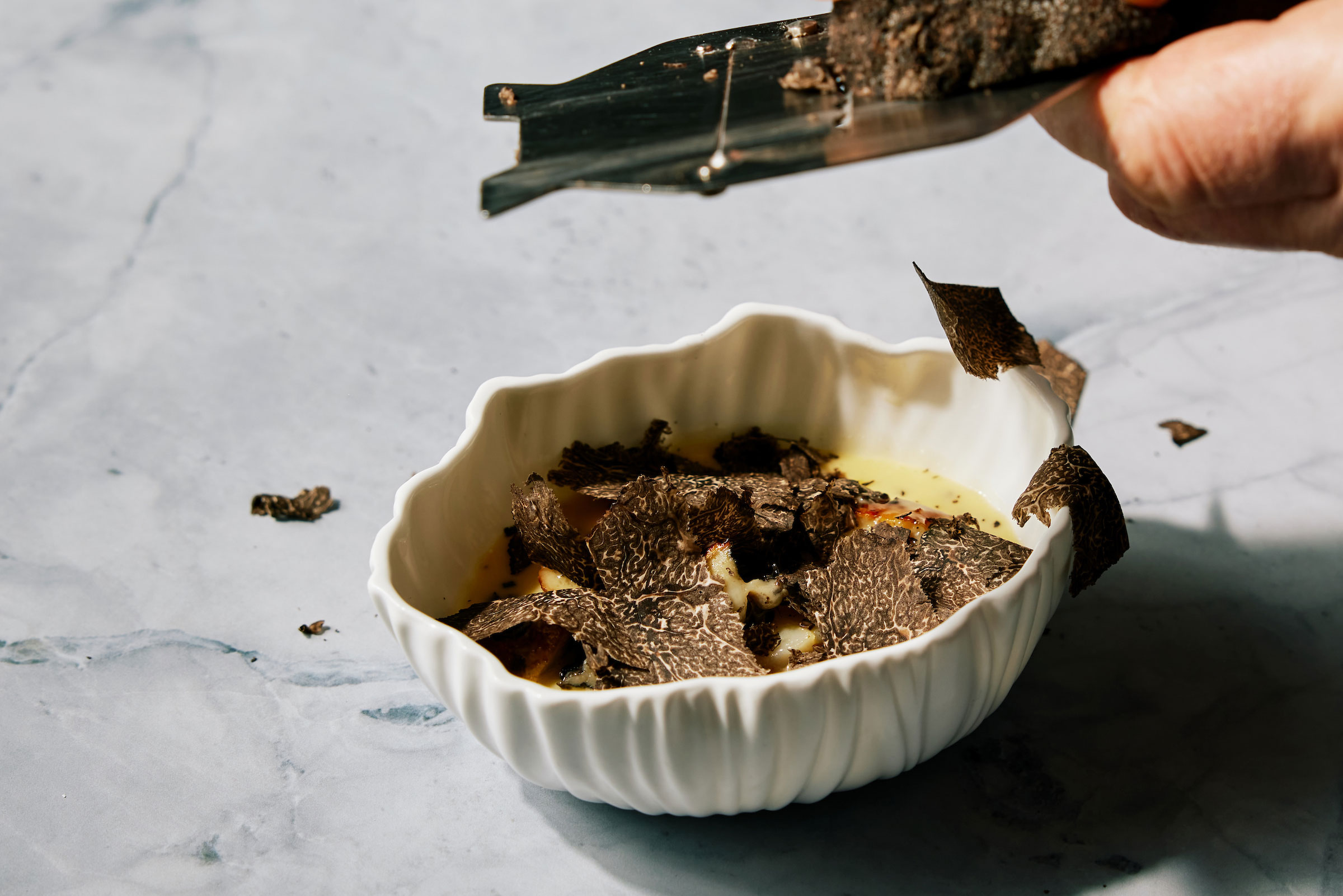 chef shaving black perigord truffles onto a bowl of monterey abalone