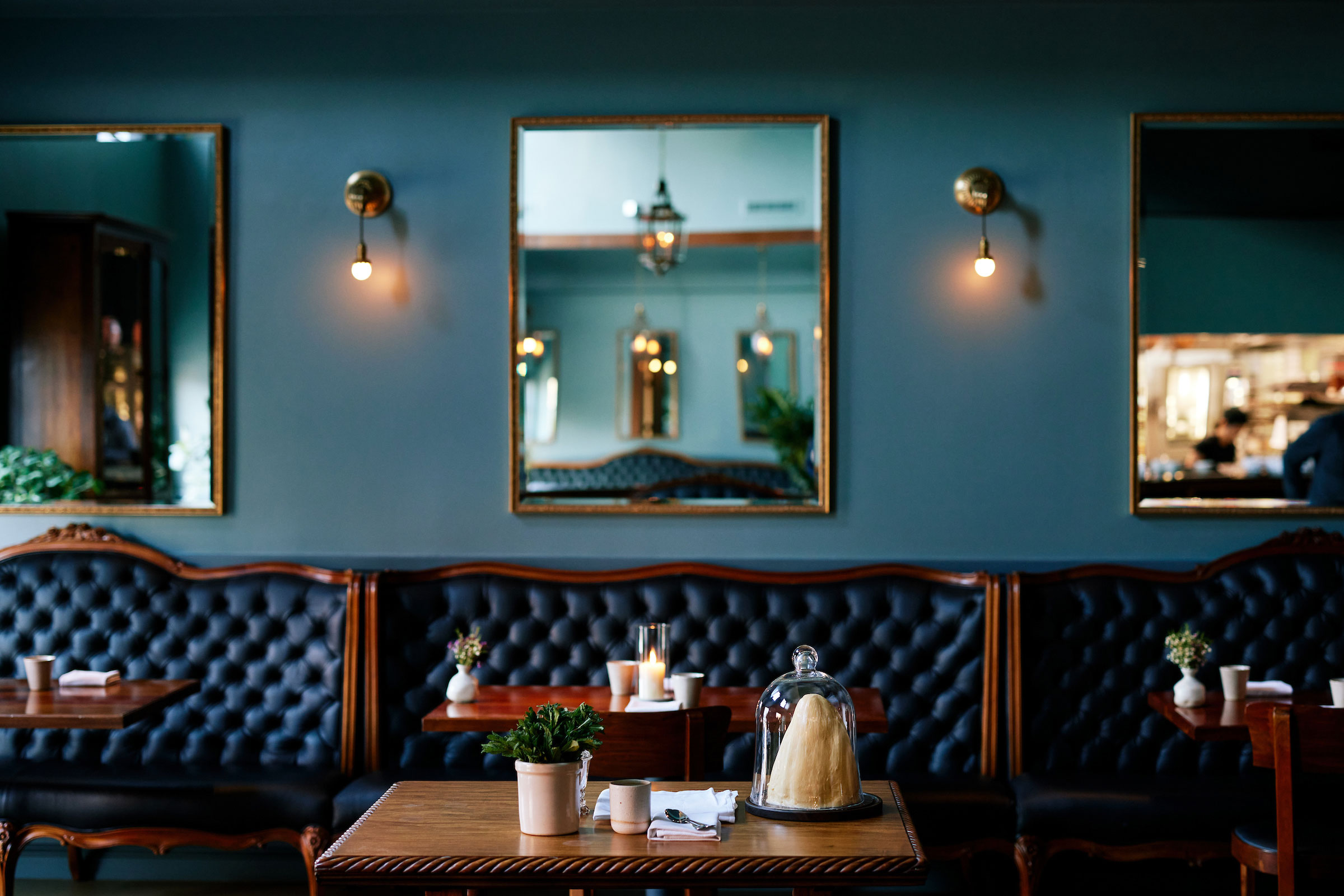 front-on shot of the dining room, with dark blue tufted banquettes, wooden tables and chairs, and sea green walls